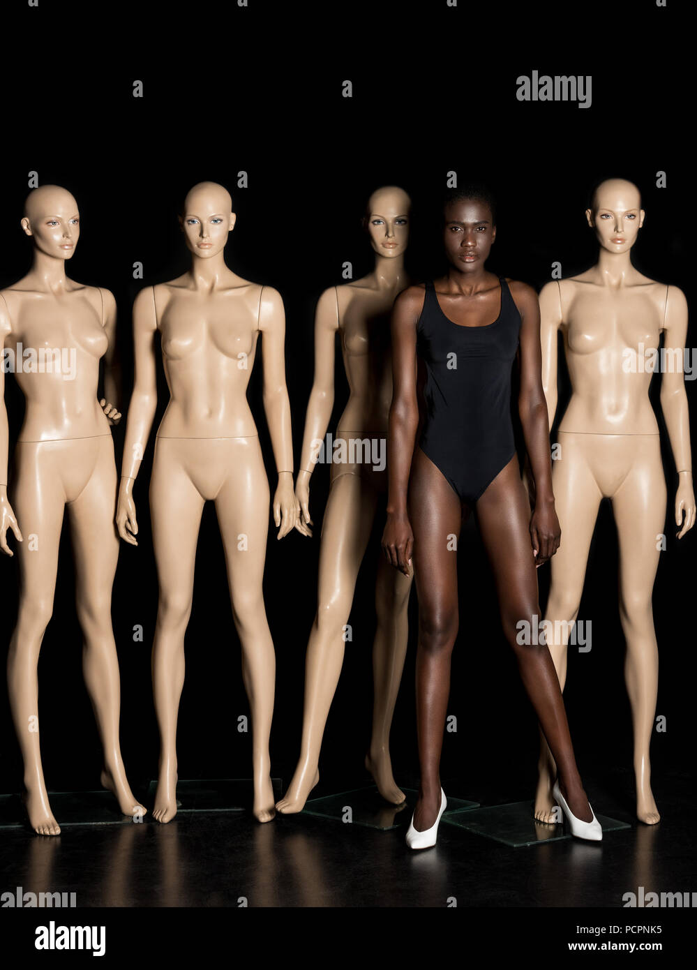 attractive african american girl in leotard standing between dummies and looking at camera on black Stock Photo