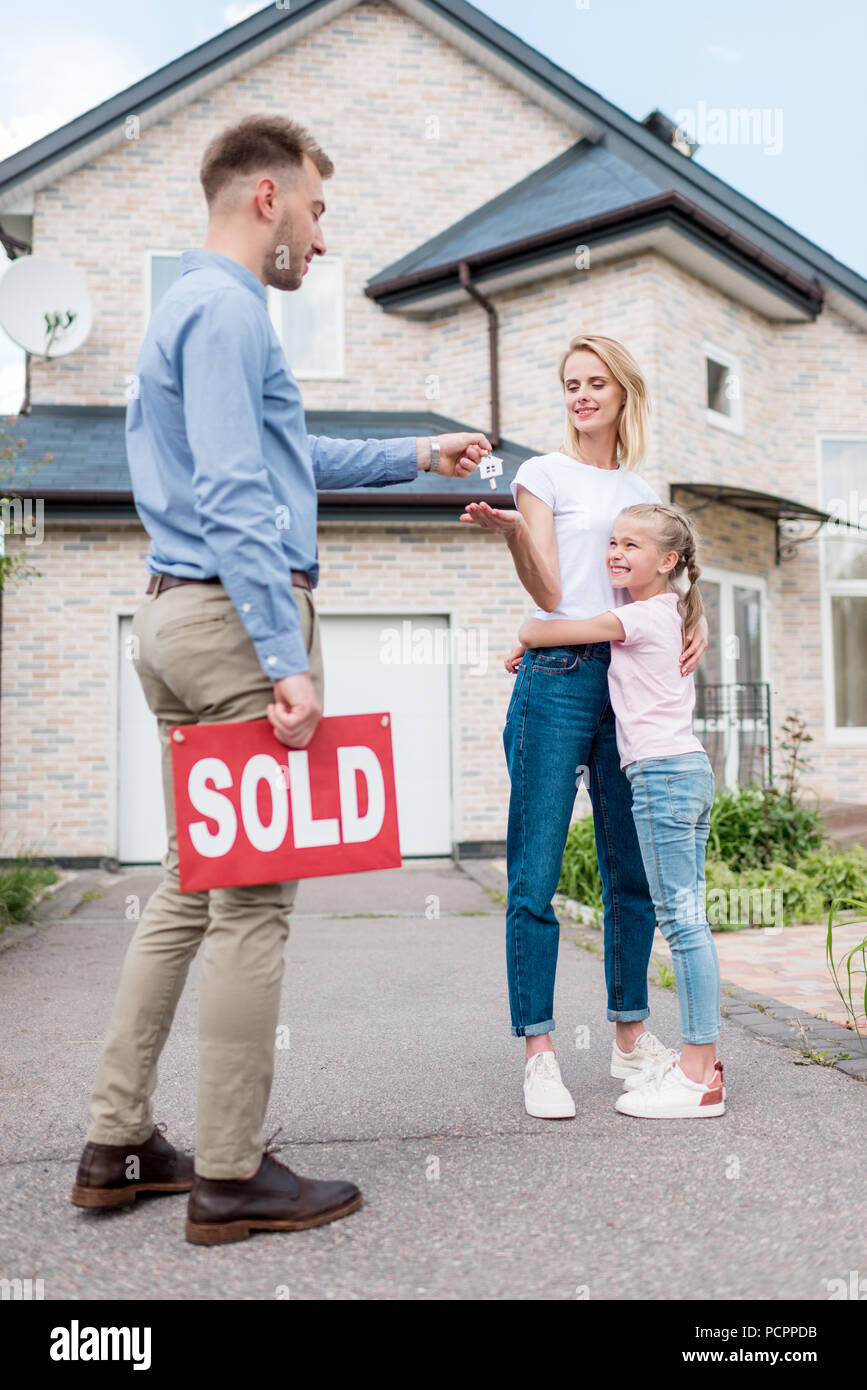 real estate agent with sold sign giving key to young woman with ...