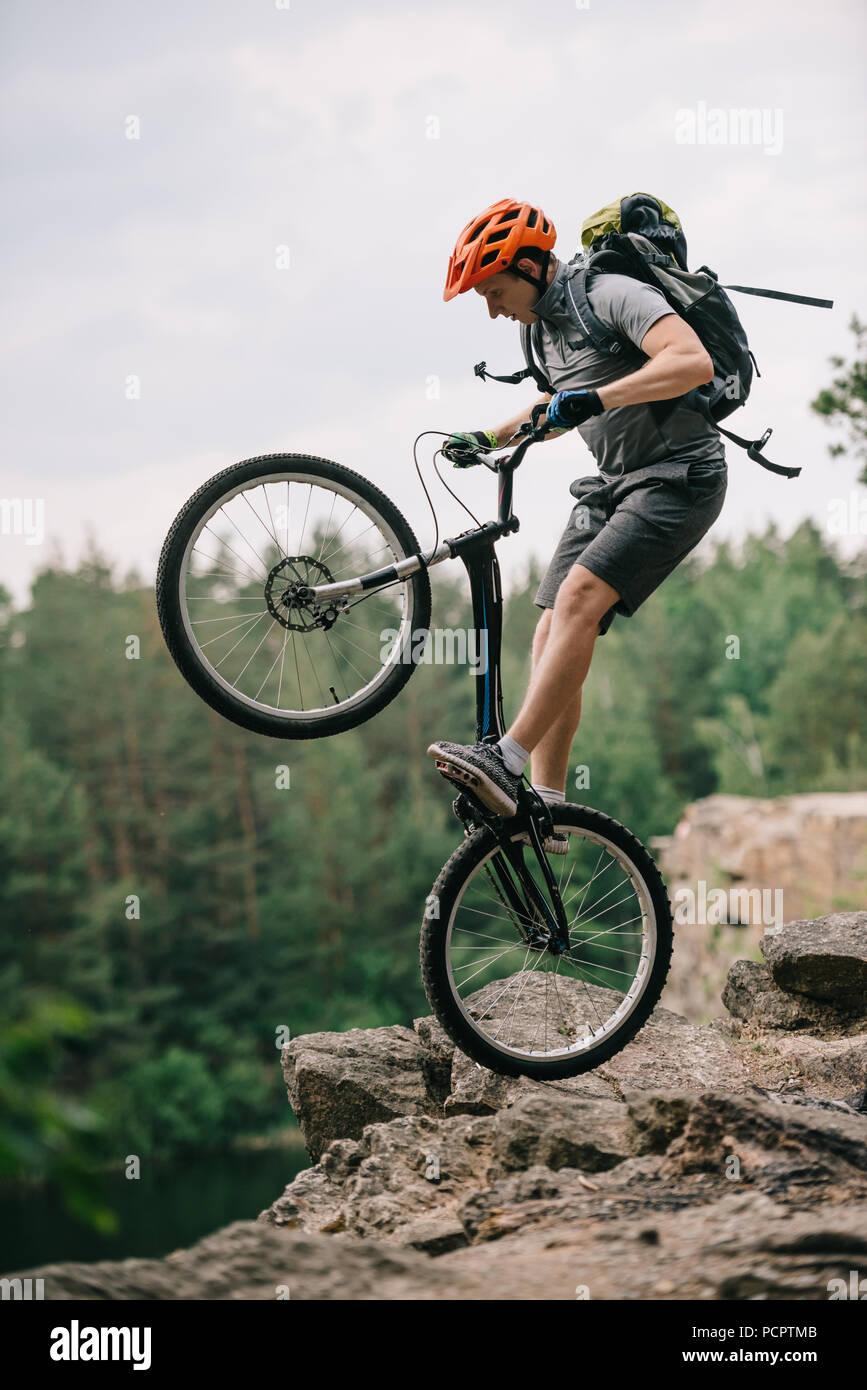 extreme trial biker standing on back wheel on rocky cliff Stock Photo