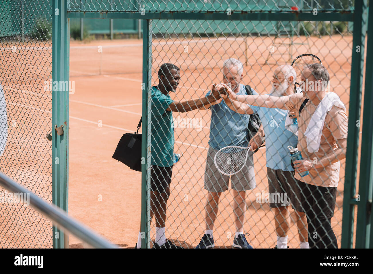 multicultural group of elderly tennis players holding hands together