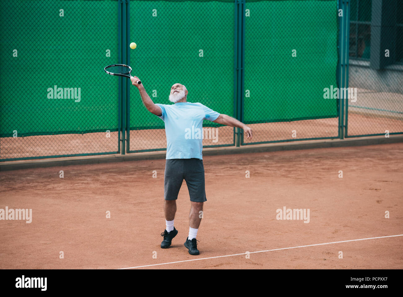 old man playing tennis on court on summer day Stock Photo