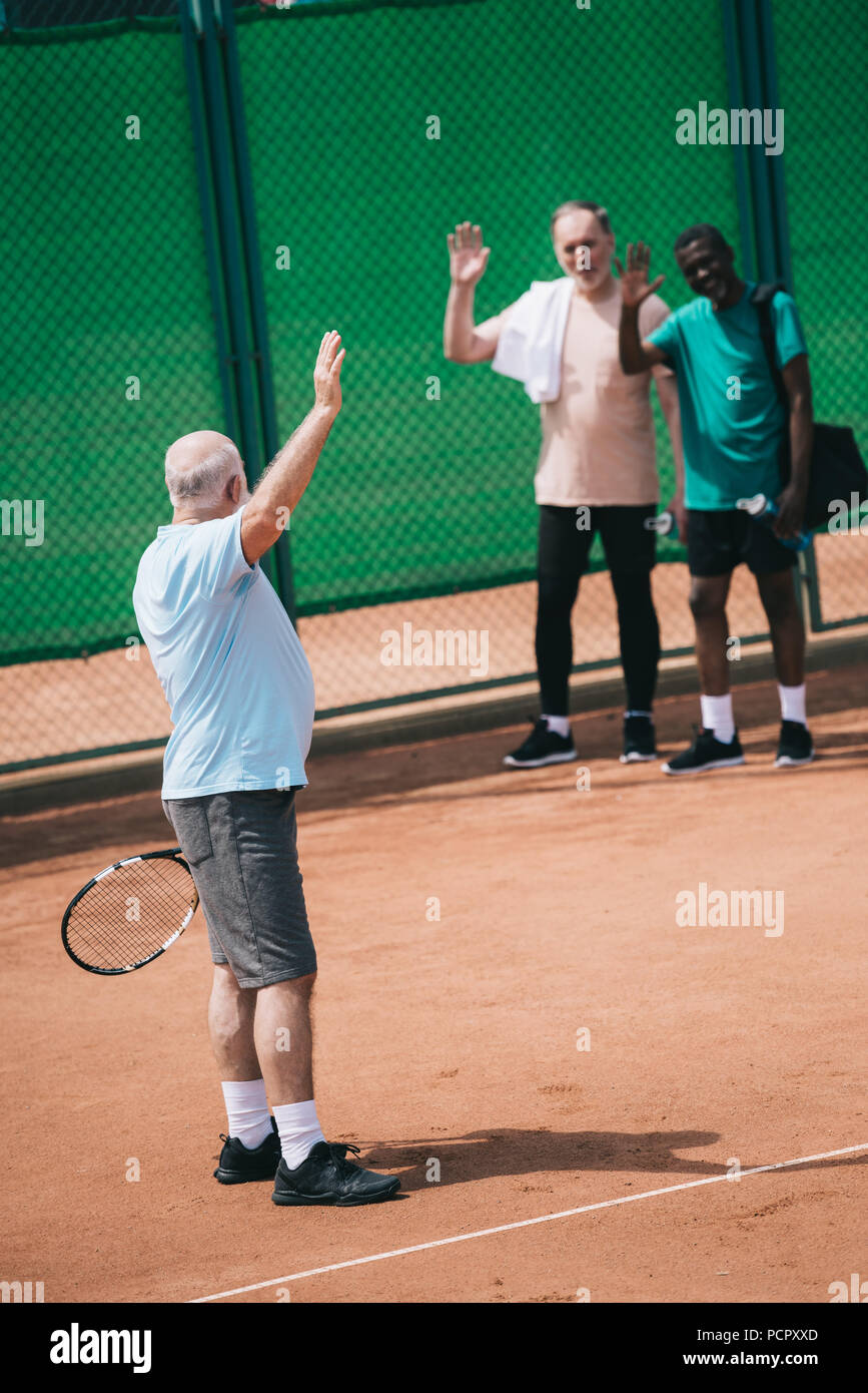 multiethnic old men greeting friend with tennis racquet on court Stock ...