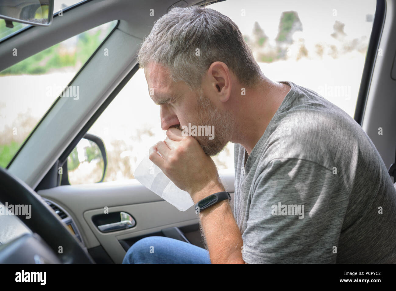 Man suffering from motion sickness in a car and holding sick bag Stock