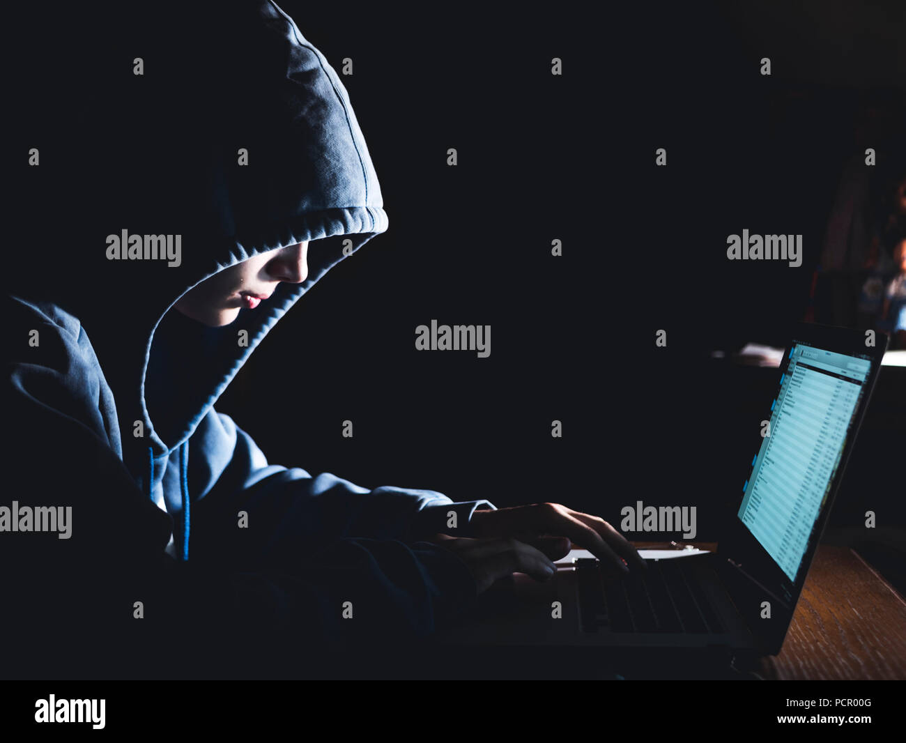 anonimous man in the hoodie in dark studio typing text online on the internet with copy space Stock Photo