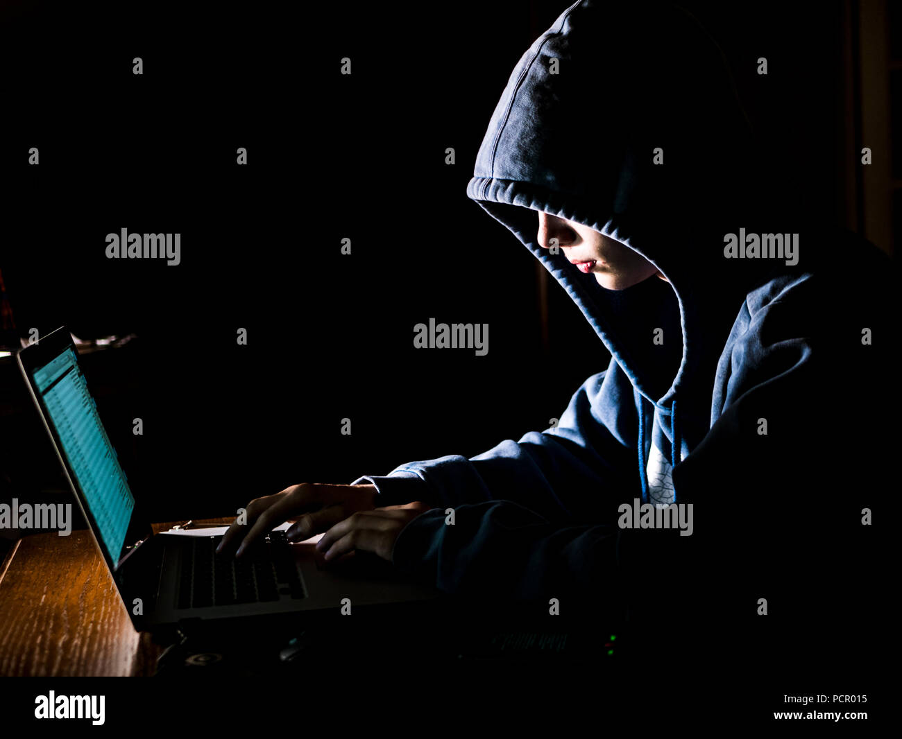 anonimous man in the hoodie in dark studio typing text online on the internet with copy space Stock Photo