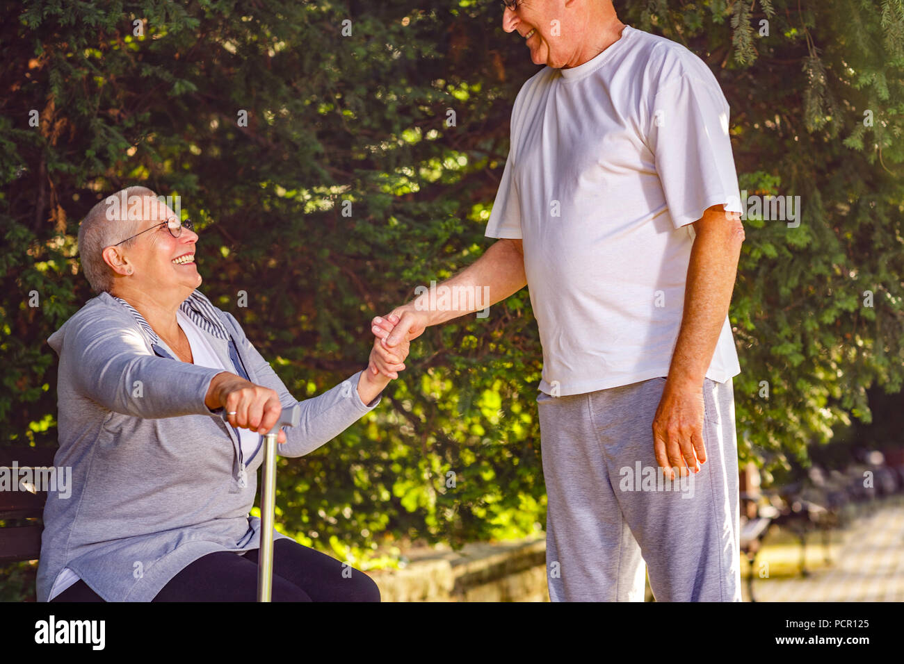 Smiling pensioner man supporting ill wife in the park Stock Photo