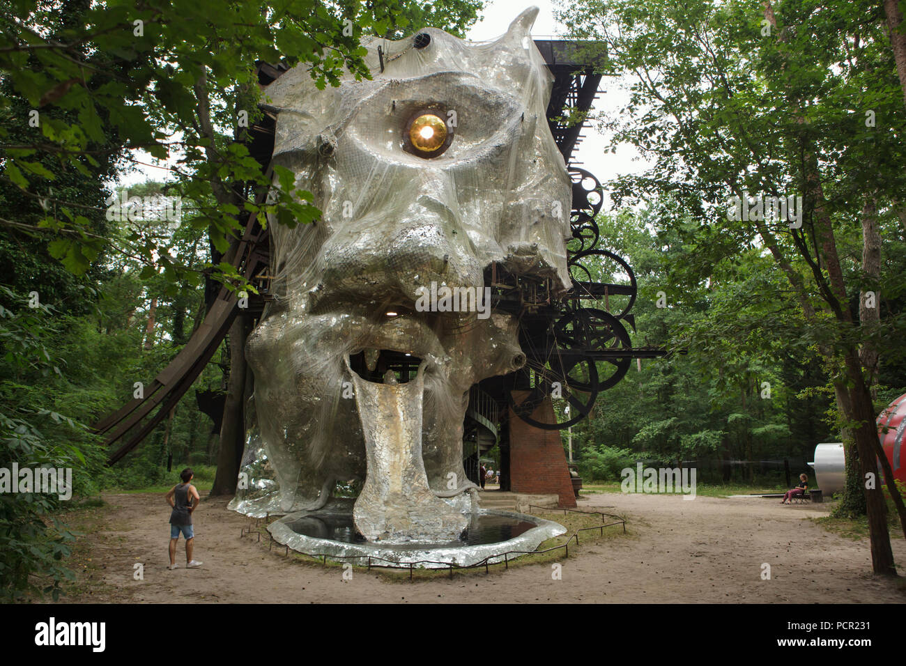 Visitor in front of the monumental kinetic sculpture Le Cyclop designed by  Swiss sculptor Jean Tinguely in cooperation with French sculptor Niki de  Saint Phalle from 1969 to 1994 in the forest