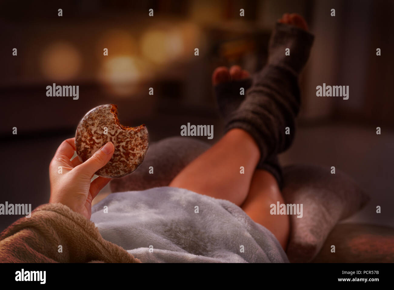 Woman with sweet gingerbread cookie and feet lying on pilow in the cozy room Stock Photo