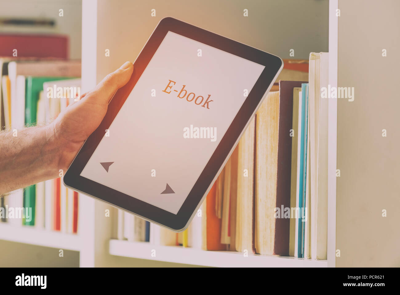Man taking modern ebook reader from a bookshelf. Stock Photo