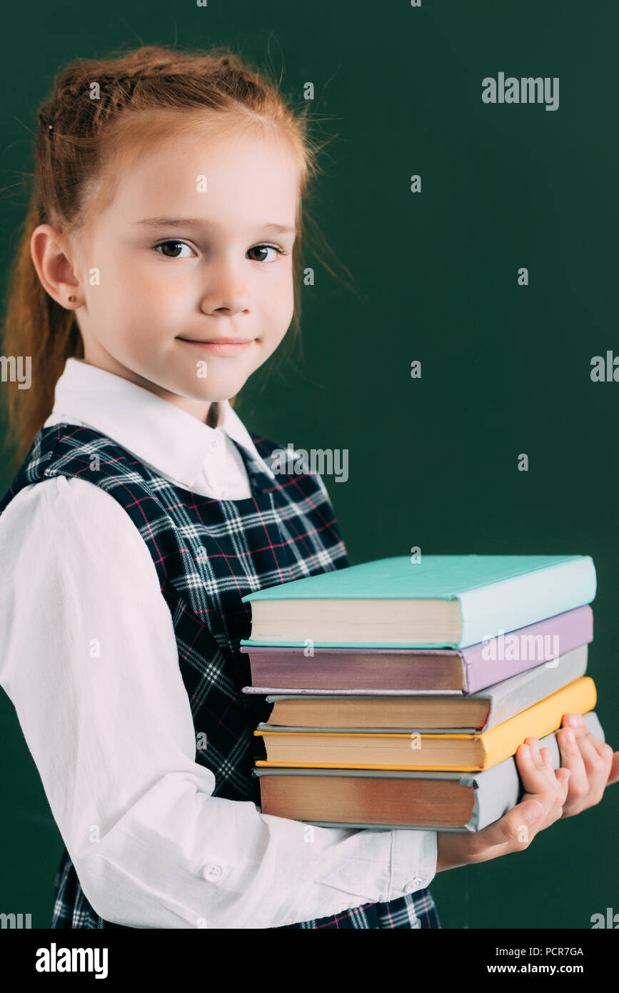 adorable little schoolgirl holding pile of books and smiling at camera ...