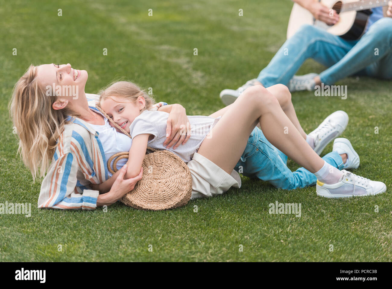 cropped shot of father playing guitar while mother and daughter hugging on grass Stock Photo