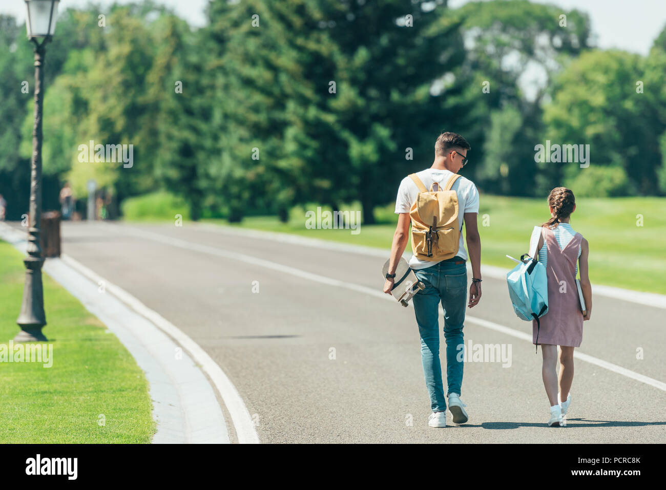 https www alamy com back view of teenage boy and girl with backpacks and skateboard walking together in park image214414835 html