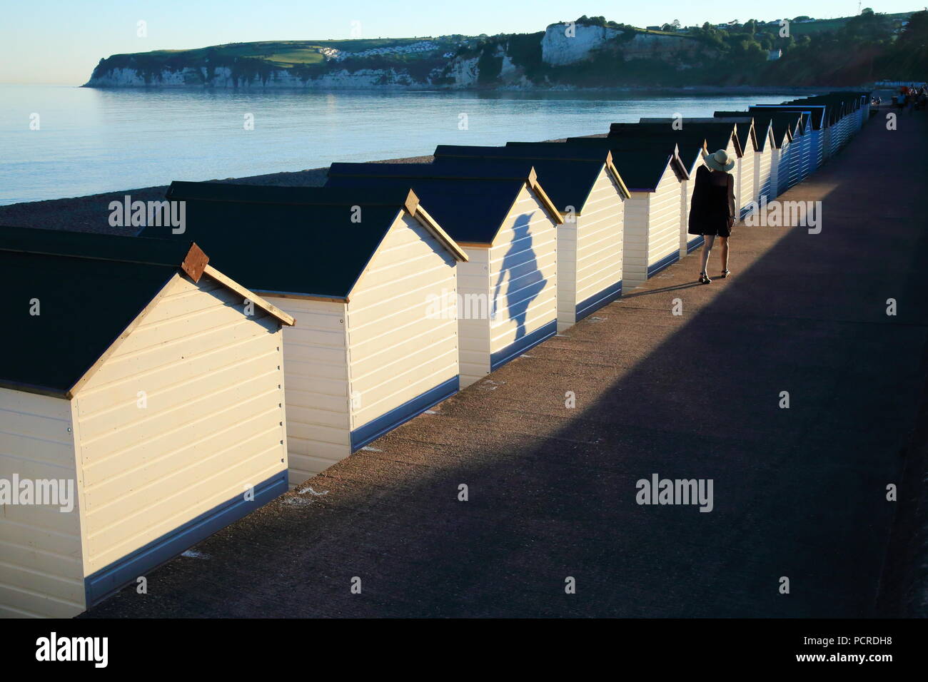 Shadows of the people passing by white beach huts in coastal town of Seaton in East Devon Stock Photo