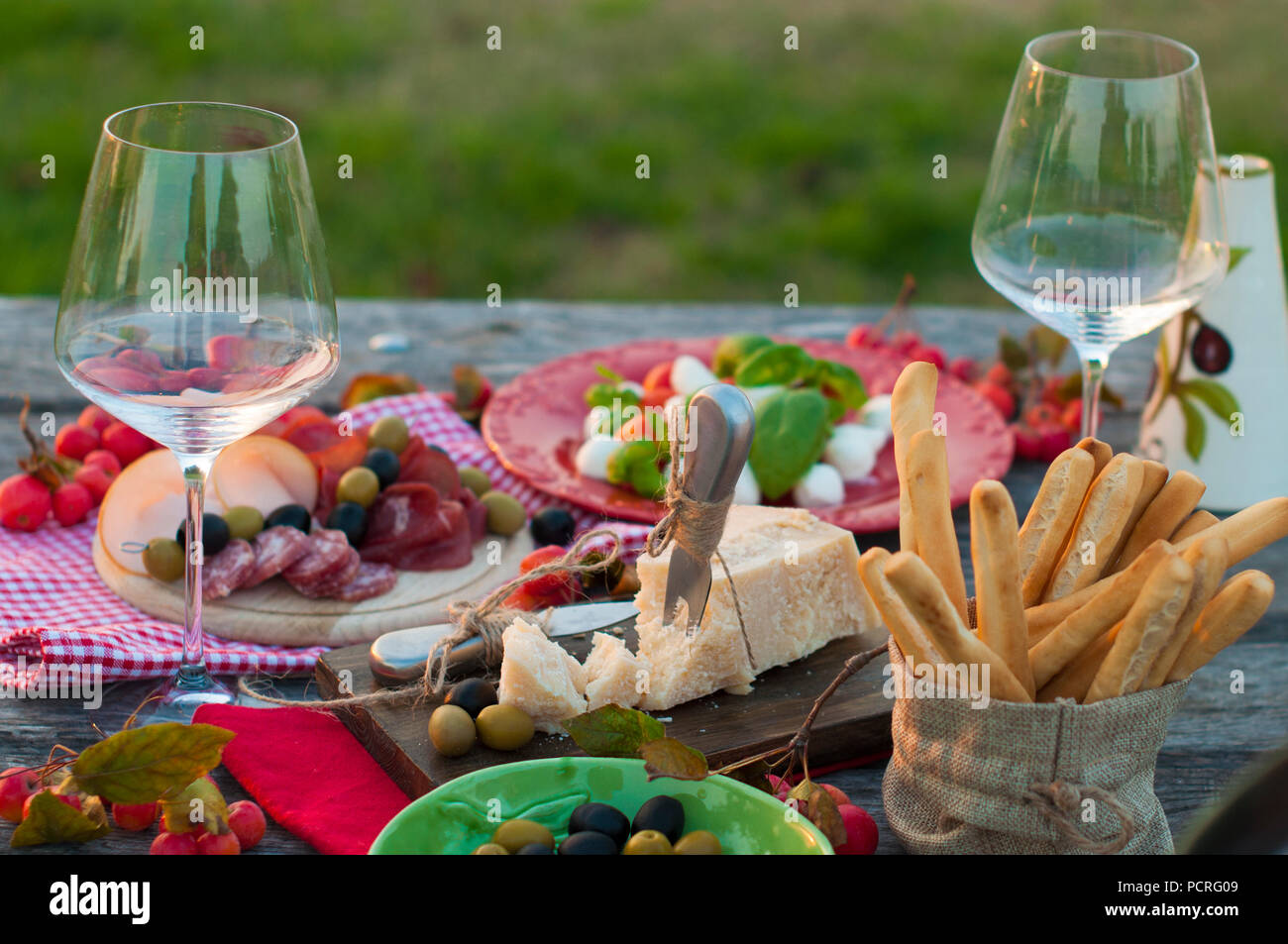 Italian picnic with red wine, Parmesan, ham, caprese salad and olives. Lunch outdoors and wooden