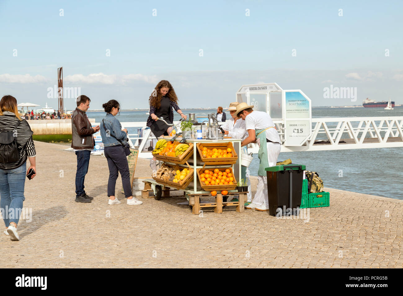 Young women operates juicer, in Lisbon Portugal. Tourists wait in line to make smoothies. Stock Photo