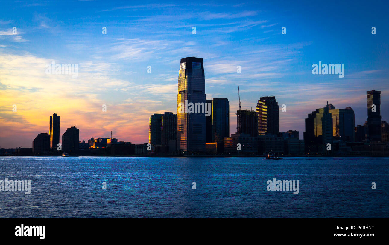 A glowing sunset of shifting clors fills the sky next to the buildings opposite Battery Park on a cold winter's evening, NYC, USA. Stock Photo