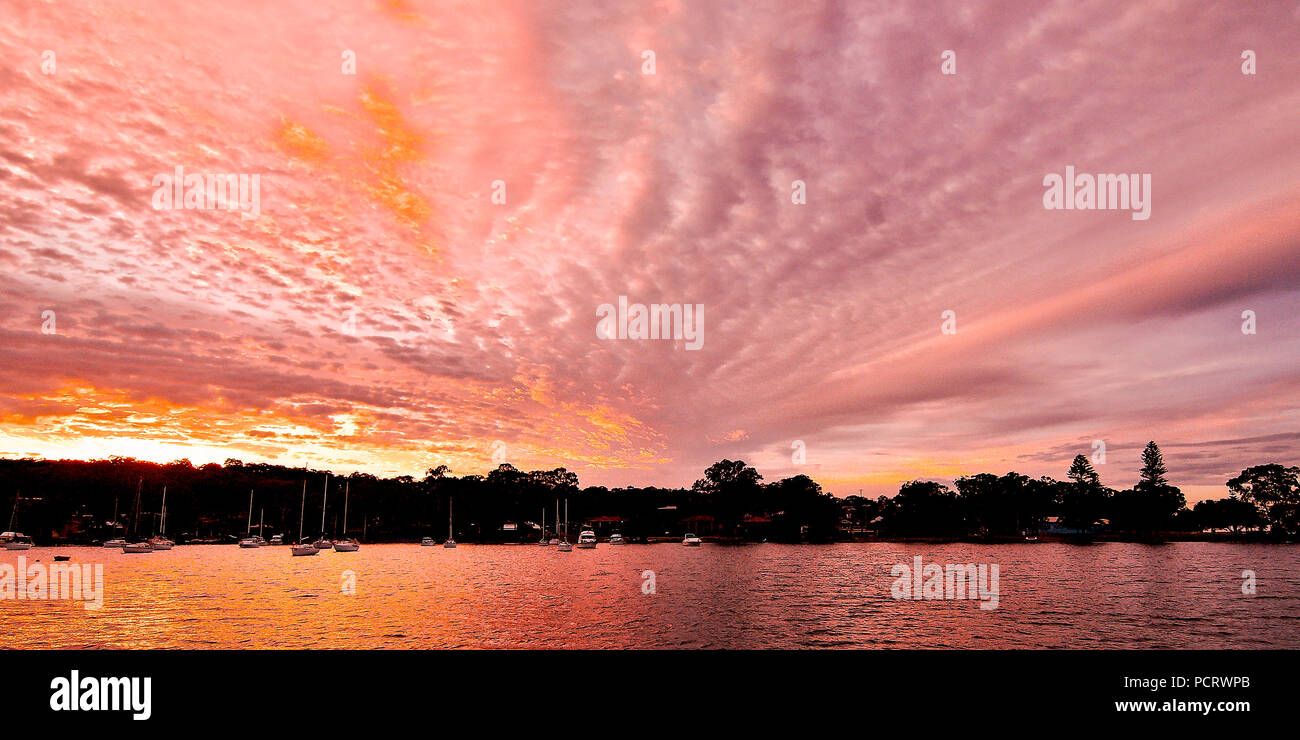 A Pastel Pink colored cloudy sunrise seascape panorama, over sea water with water reflections. Queensland, Australia. Stock Photo
