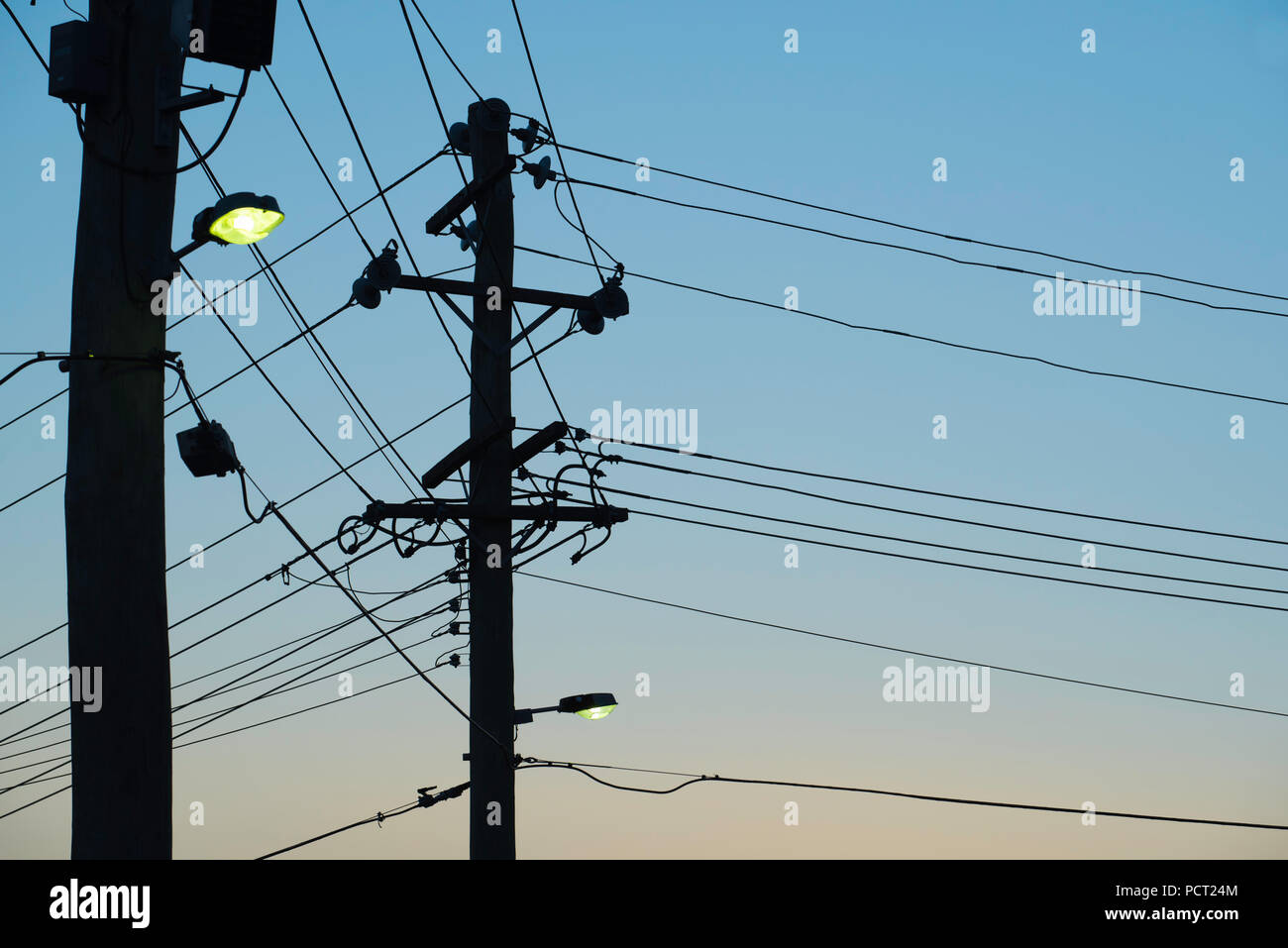 Two Australian timber electricity power poles with street lights turned on and wires attached at dusk Stock Photo