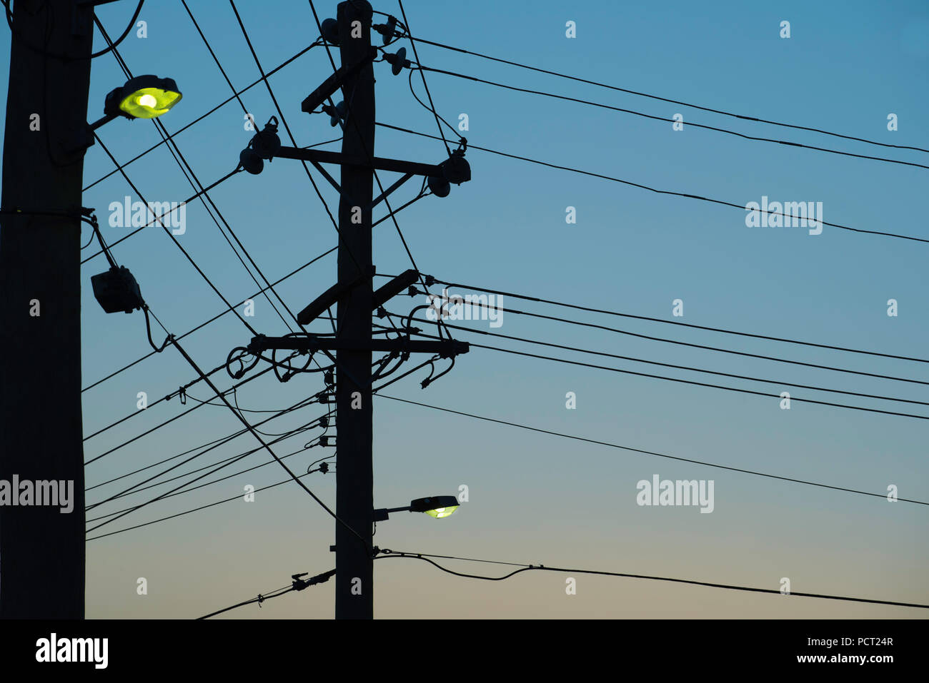 Two Australian timber electricity power poles with street lights turned on and wires attached at dusk Stock Photo