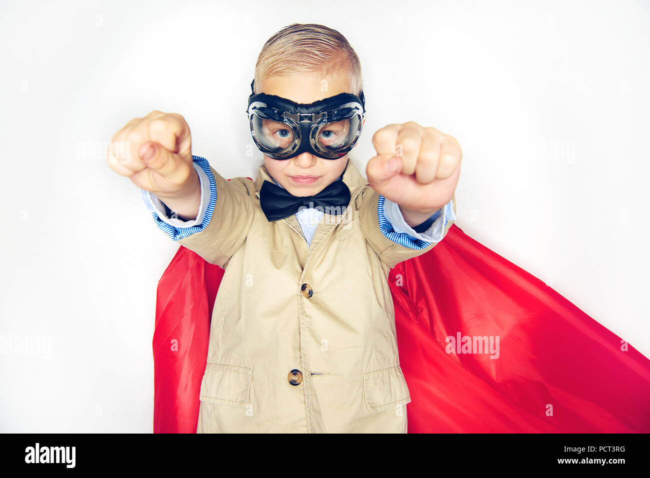 Cute little boy superhero in a suit and bowtie wearing a red cape and