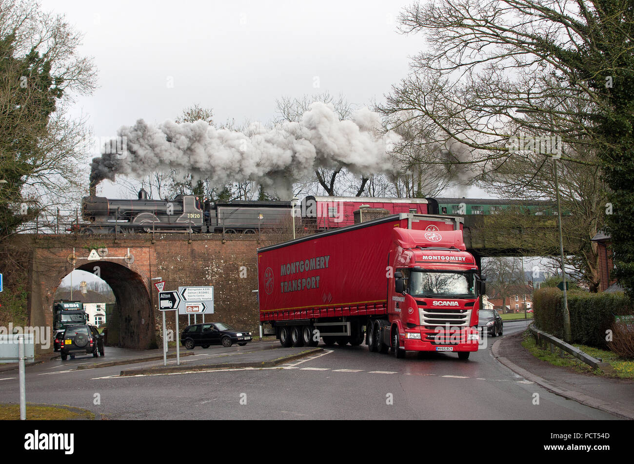 LSWR T9 Class steam engine No 30120, built in the 19th century, crosses the brick arch at The Butts, Alton as a 21st century lorry passes beneath Stock Photo