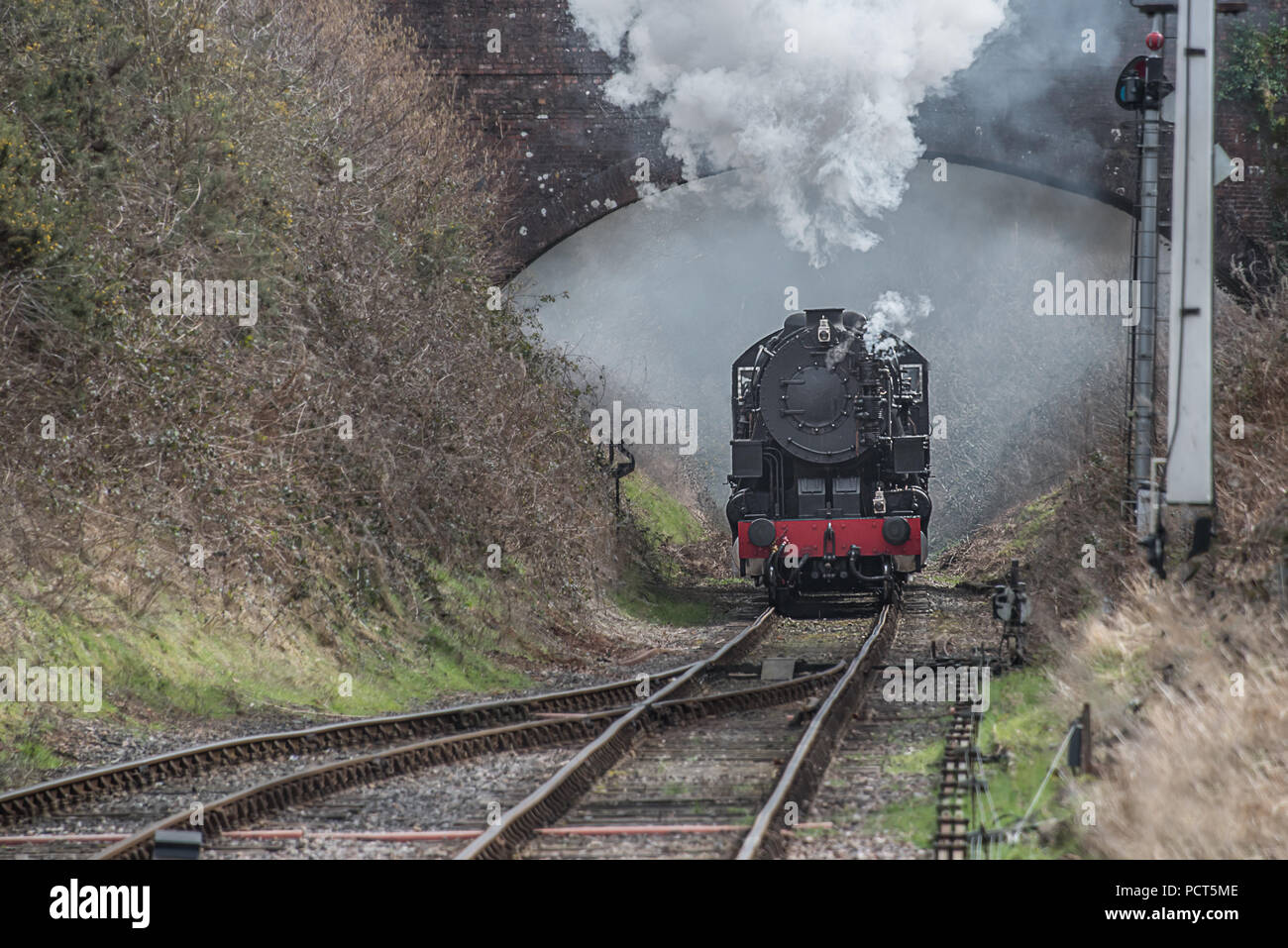 Looking down the track as a steam locomotive heading forward. Taken as the train goes under a bridge. The steam and smoke are bellowing from the chimn Stock Photo