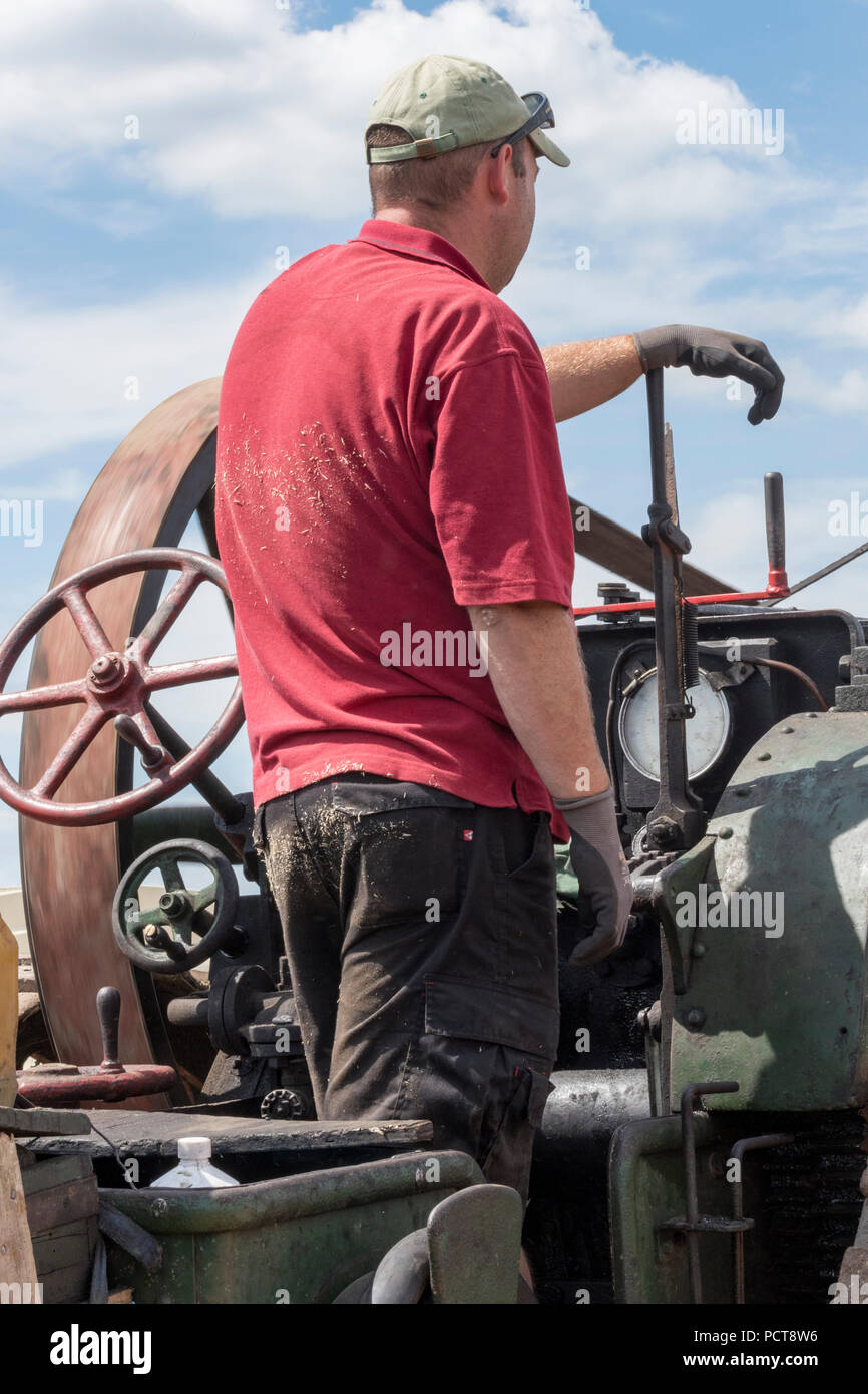 a steam enthusiast driving on the footplate of a large vintage steam roller or traction engine at at steam rally on a summers day. Stock Photo