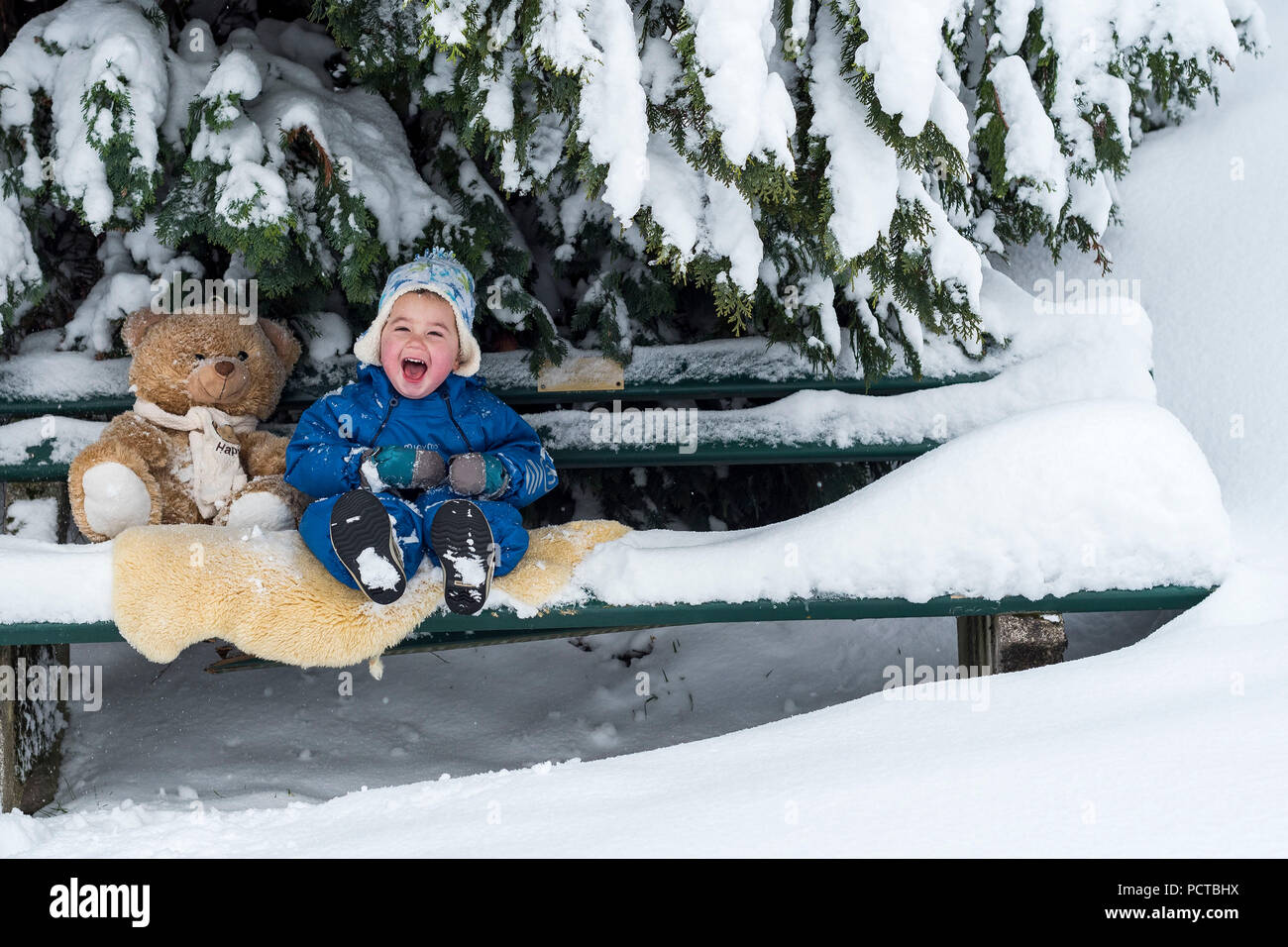 Little boy sitting with teddy bear on a bench and laughing in the ...