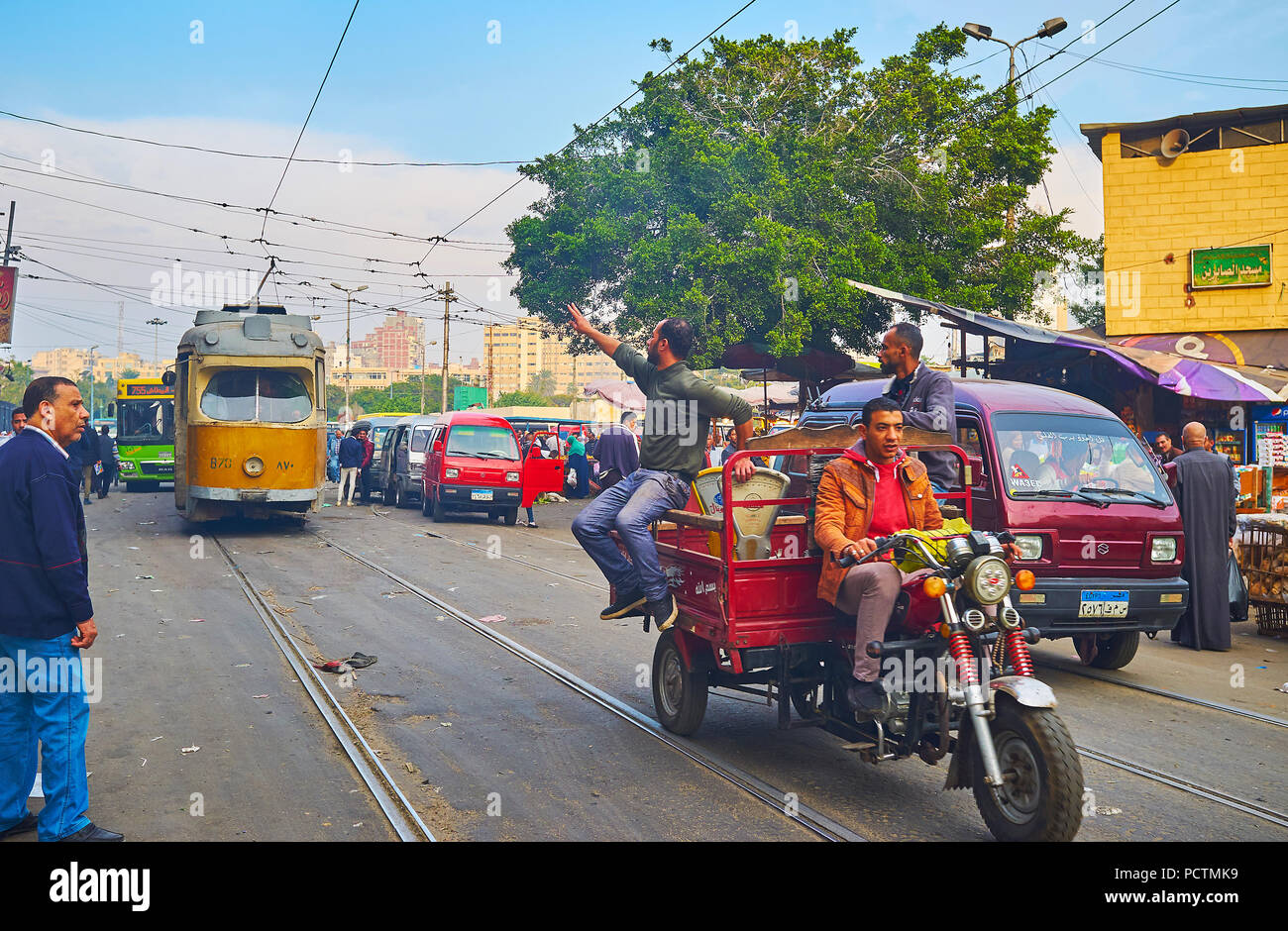 ALEXANDRIA, EGYPT - DECEMBER 18, 2017: The market vendors ride on motorcycle cargo trailer along the tramway in Sharif Avenue with vintage tram on the Stock Photo