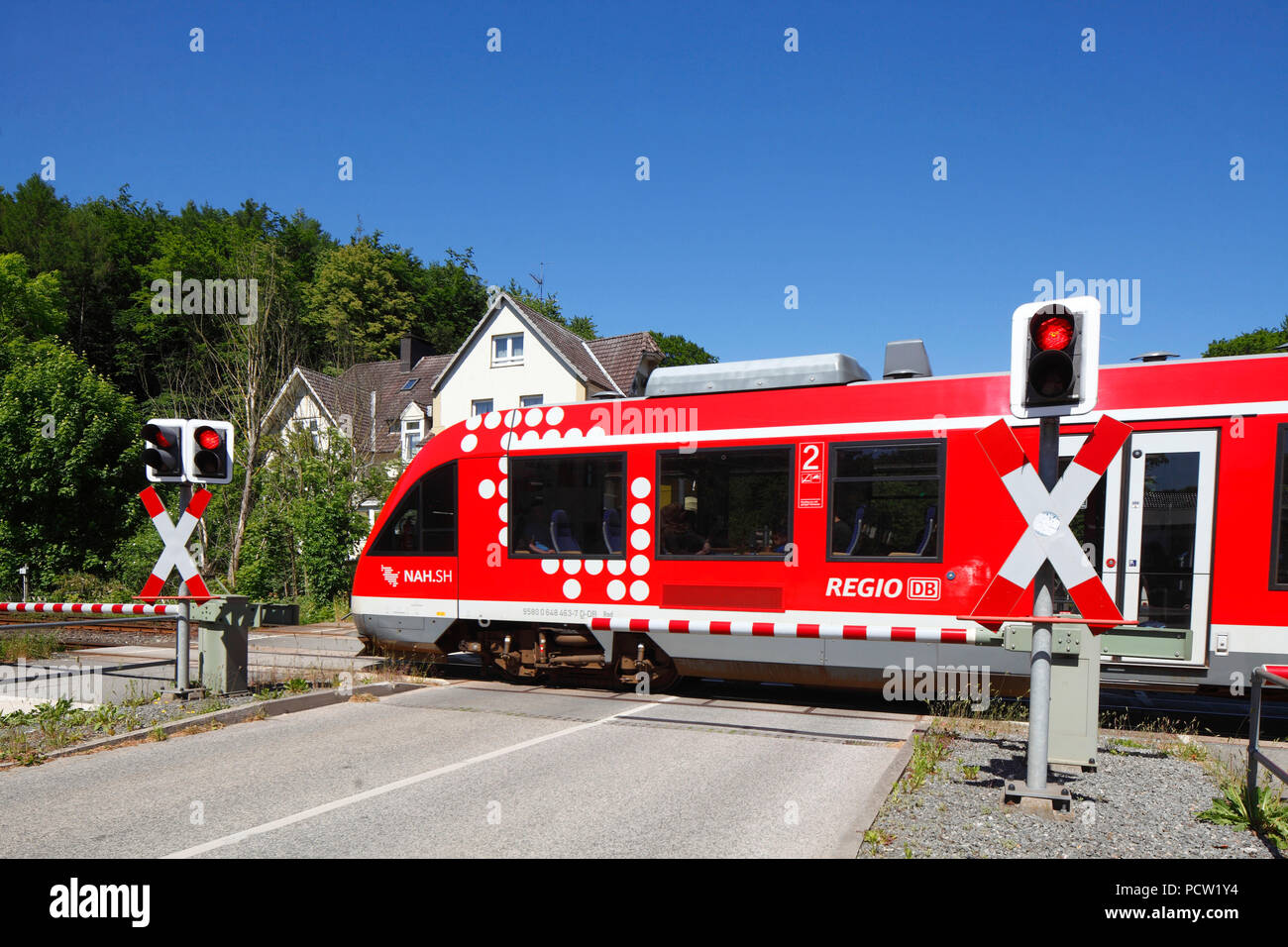 Passing red local train, restricted railroad crossing with closed gate in the Hindenburgallee, Bad Malente-Gremsmühlen, Malente, Schleswig-Holstein, Germany, Europe Stock Photo