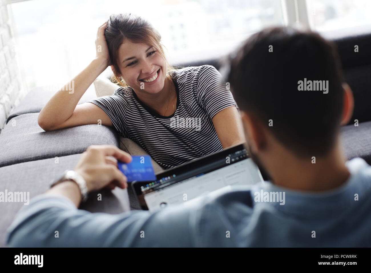 Young hispanic couple laying on couch at home, using a tablet PC and credit card for online purchase. Stock Photo