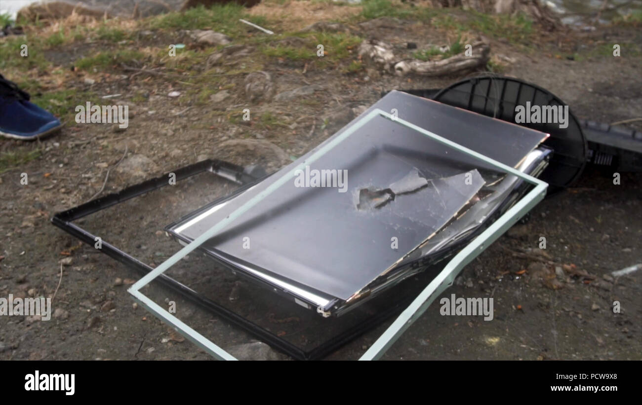 Man with a hammer breaks the monitor in nature. Smashed old computer
