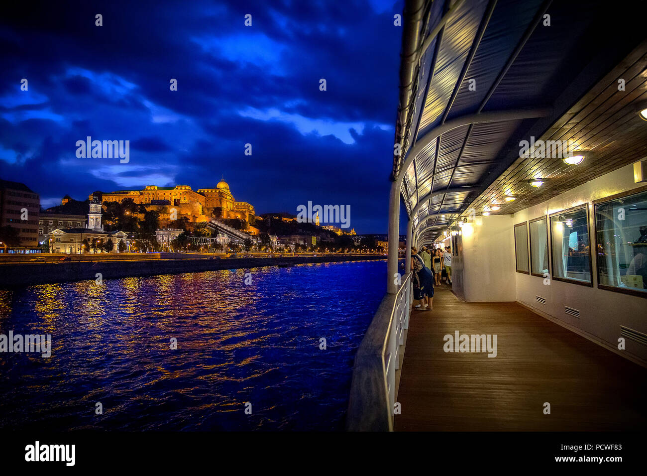 The panorama of Budapest is admired by tourists from the deck of the cruise ship at night. Stock Photo