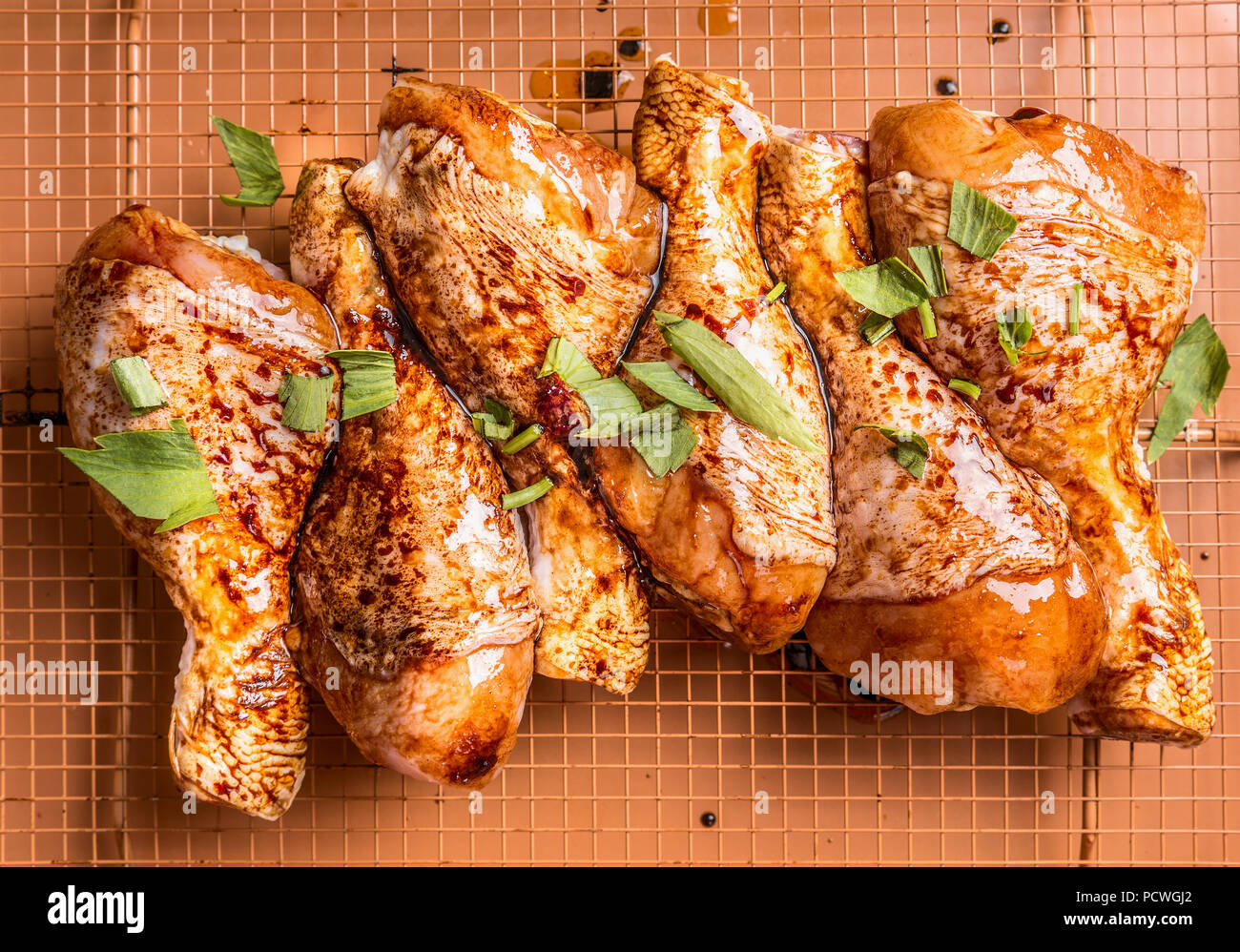 Close up of Raw marinated chicken drumsticks on grill grid with ingredients, herbs and spices