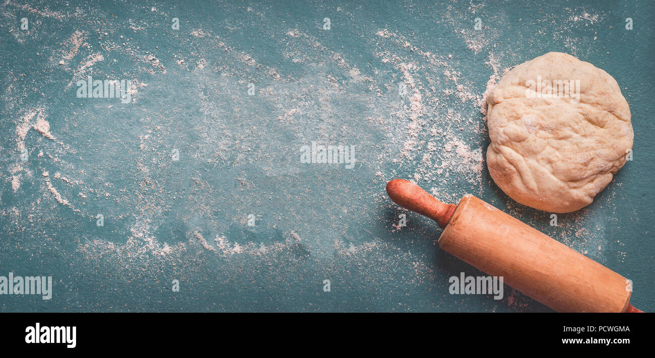 Dough with rolling pin on blue rustic background with flour, top view
