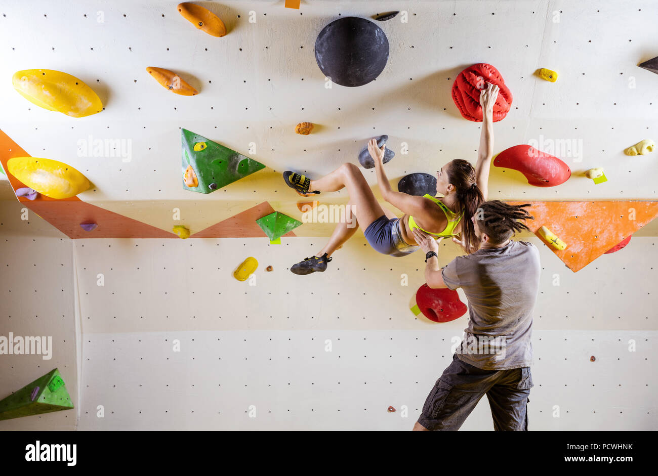 Rock climbers in climbing gym. Young woman climbing bouldering problem (route) on overhanging
