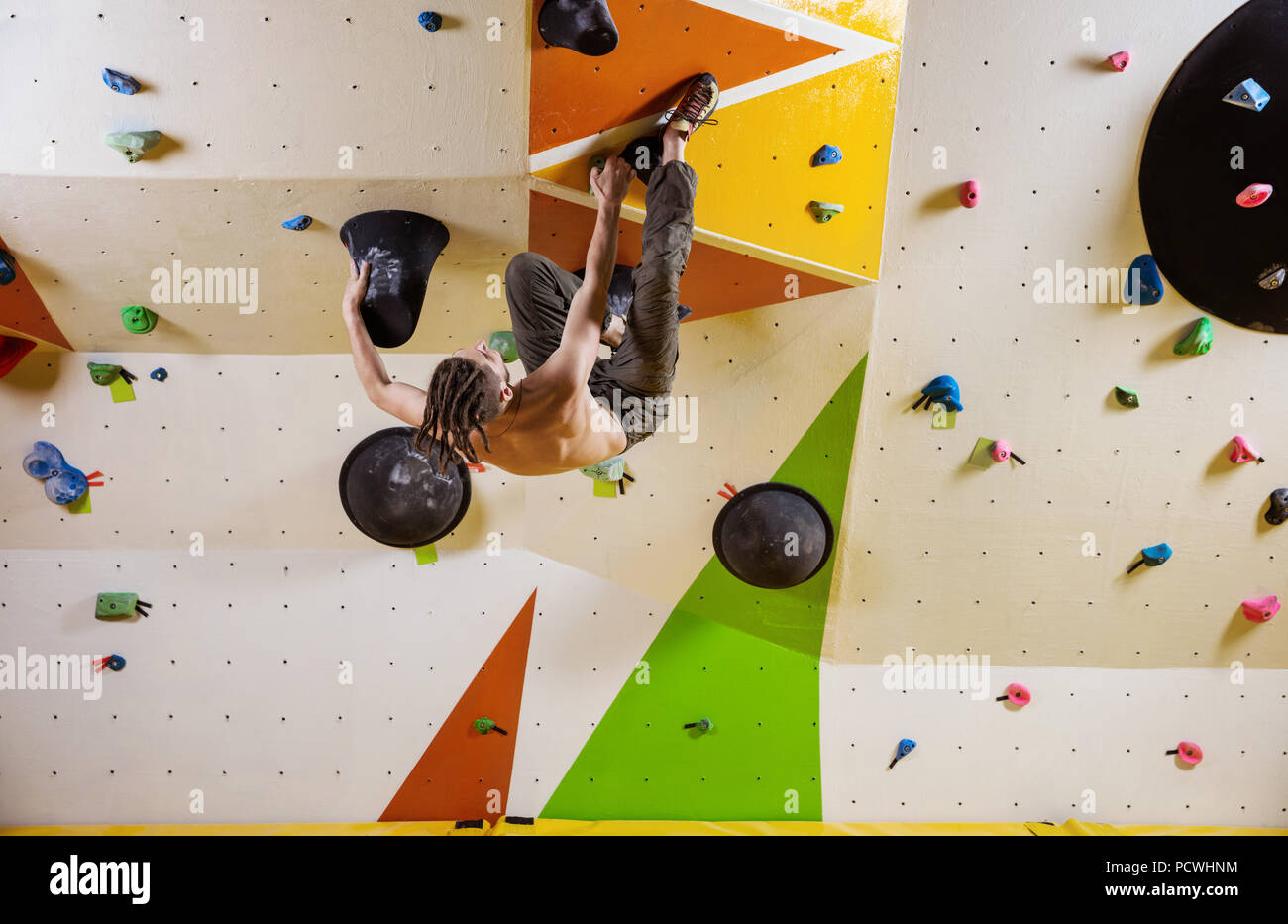Young man climbing challenging bouldering route. In indoor climbing gym ...