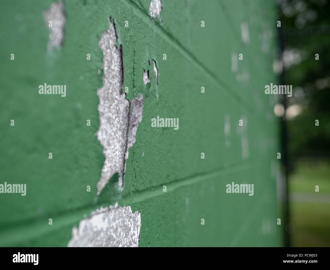 Angled view of paint peeling off of green wall in the outdoors Stock