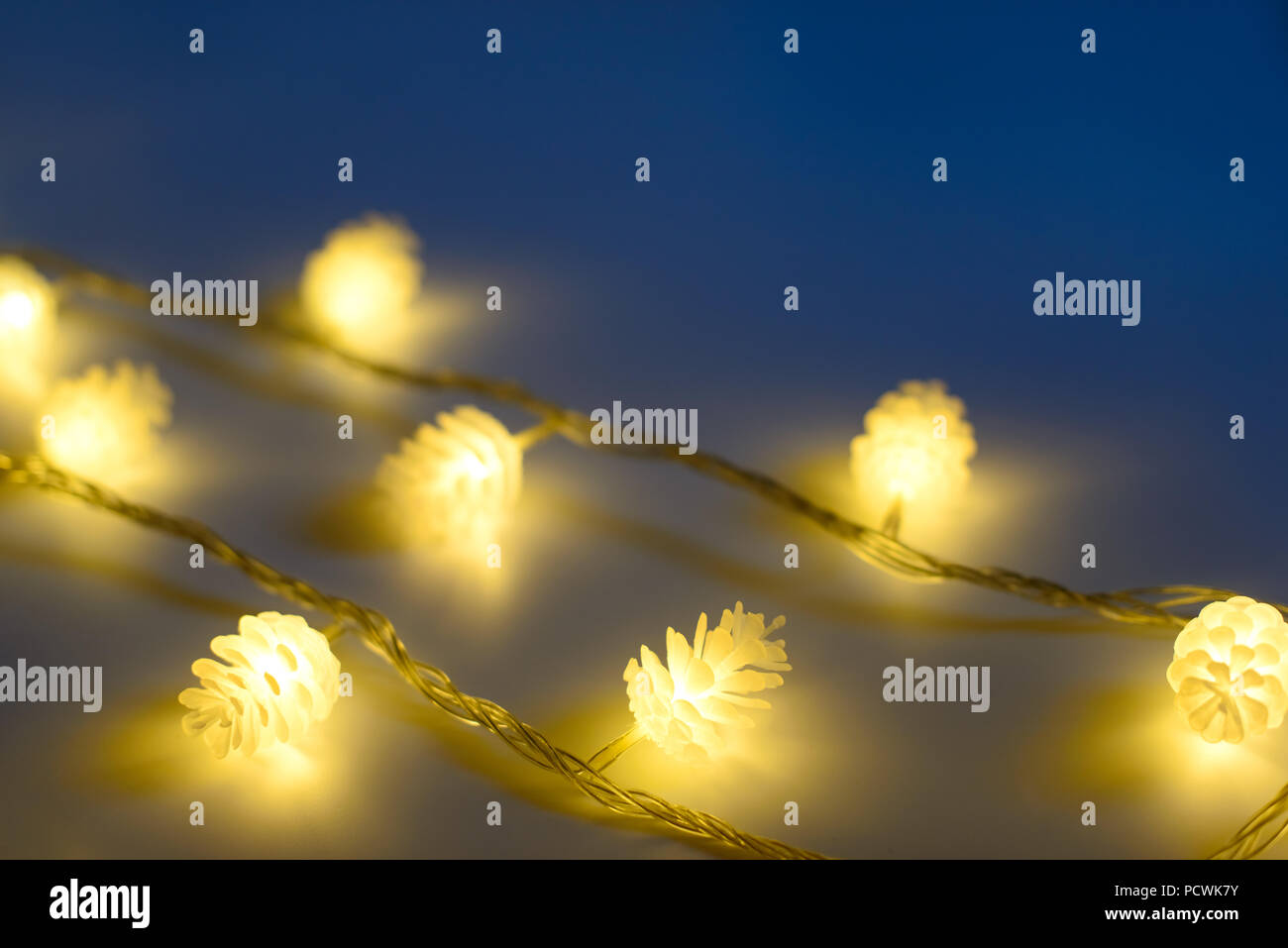 Blurred yellow christmas lights in shape of cones in three rows on dark background , low depth of focus. Stock Photo