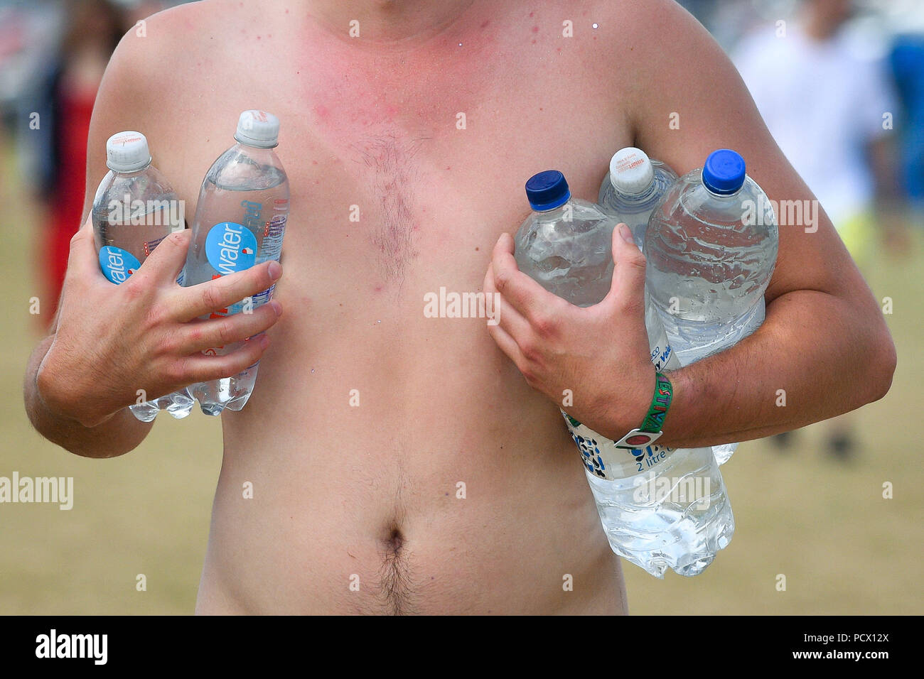 A man carries lots of refilled water bottles in the hot sunny weather during Bestival at the Lulworth Estate in Dorset. Stock Photo