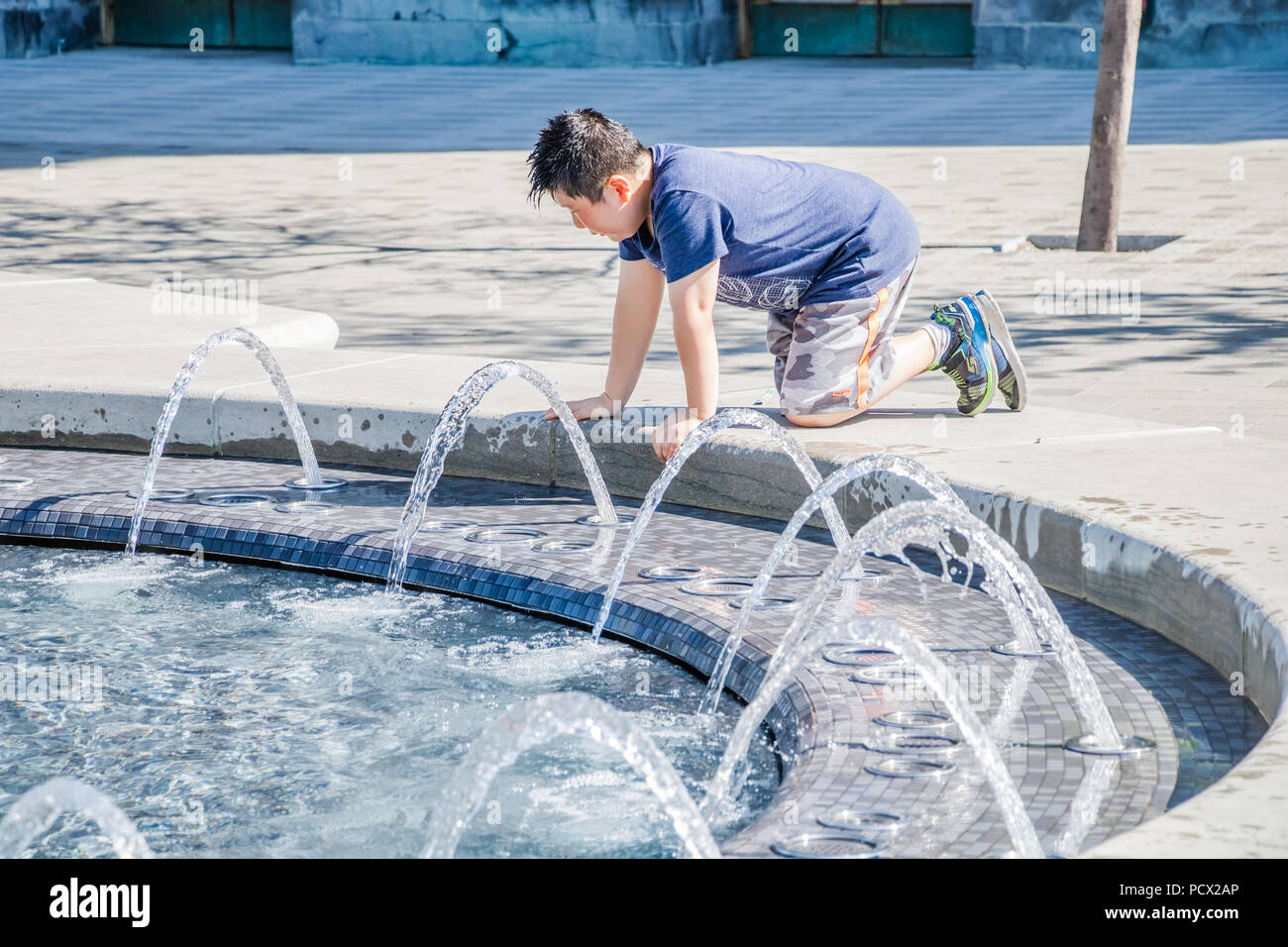 young boy trying to cool off in front of water fountain Stock Photo