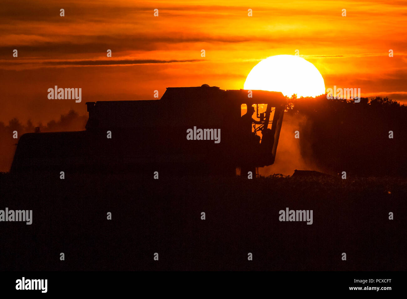 Staffordshire, UK. 4 August 2018.  A combine harvester working a field during a stunning red sunset near Abbots Bromley, Staffordshire, UK, on the evening of the 4th August 2018. Photograph by Richard Holmes. Stock Photo