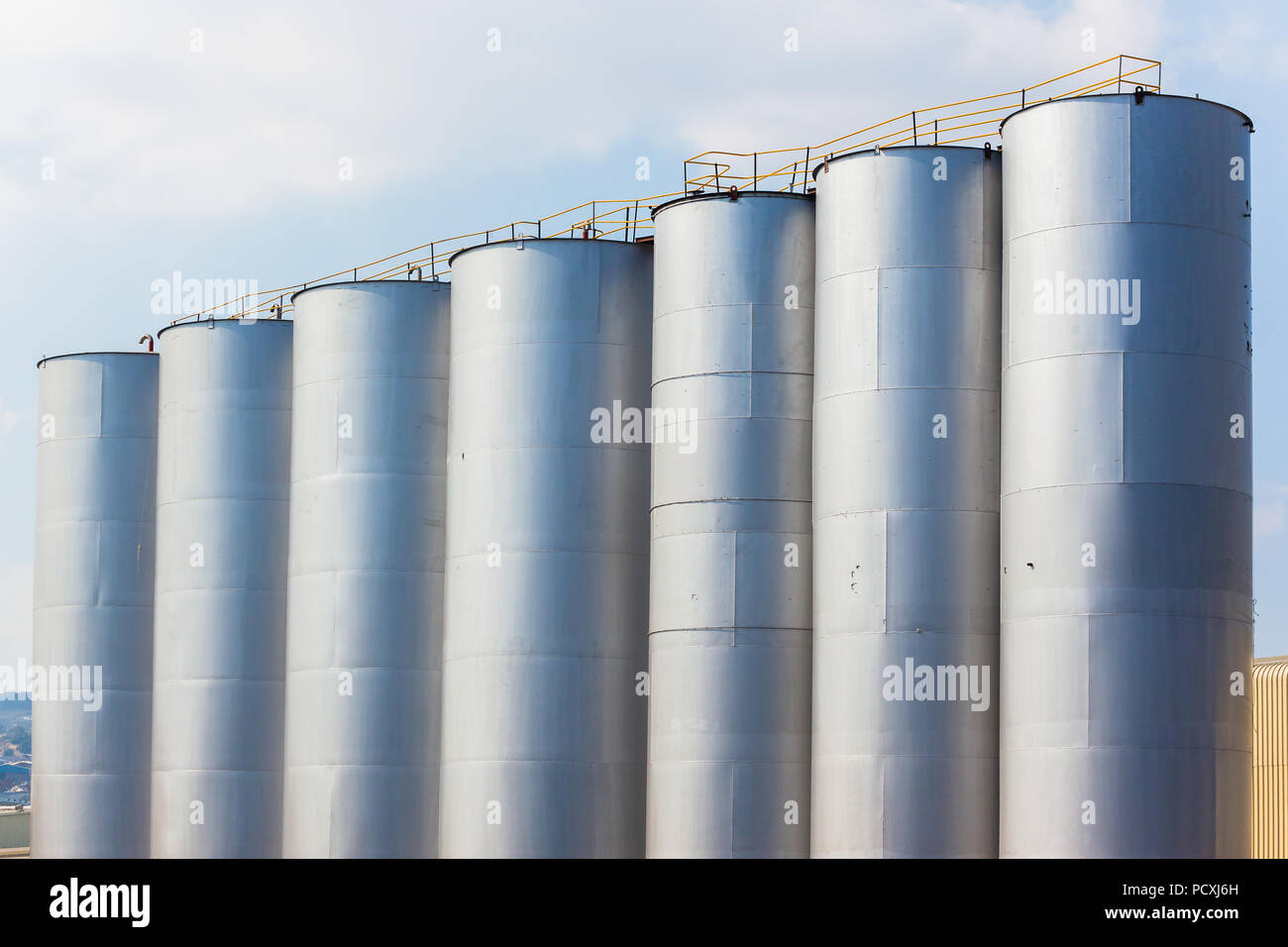 Seven steel silver painted silo tall storage tanks with walkway on top Stock Photo