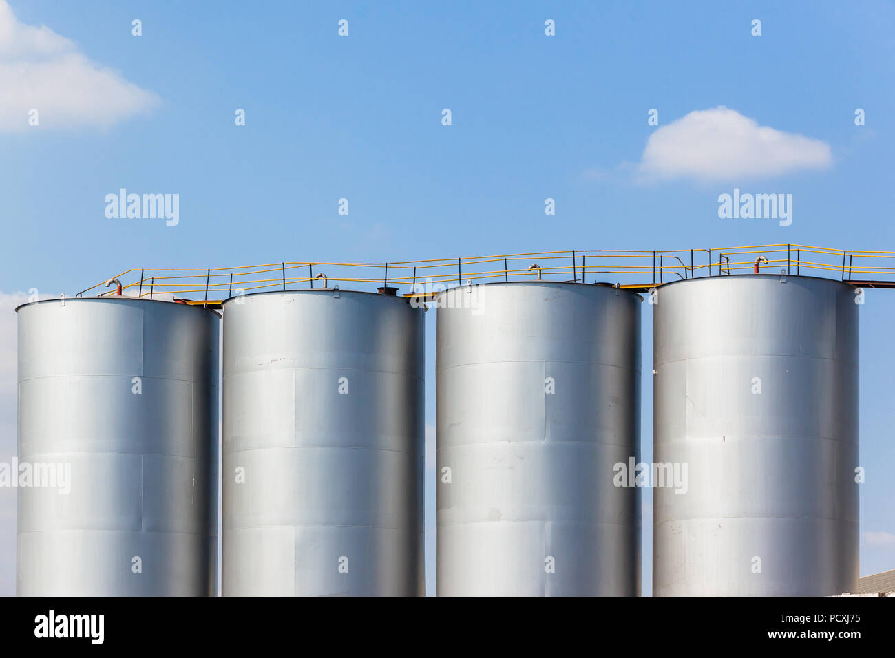 Four steel silver painted silo tall storage tanks with walkway on top Stock Photo