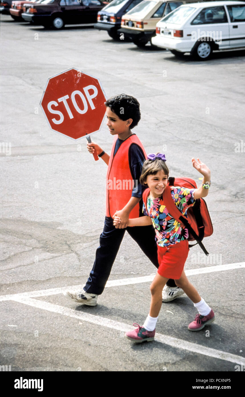 Crossing guard Sixth grader helps little girl across parking lot at school Stock Photo