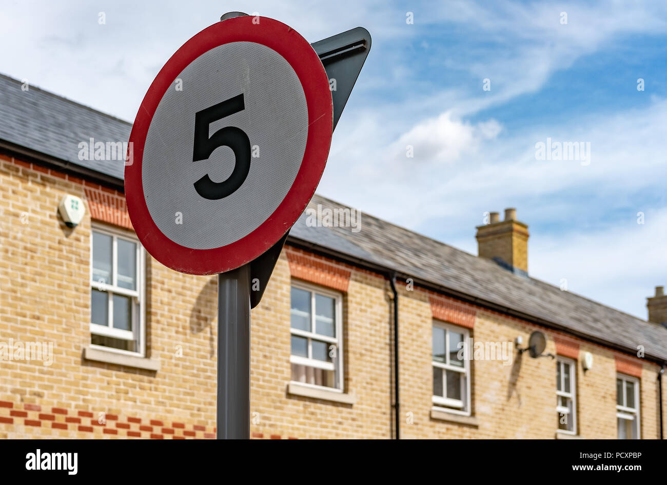 Isolated image of a 5mph speed limit sign seen within a town centre. The background shows new terraced houses located in a quiet street in the UK. Stock Photo