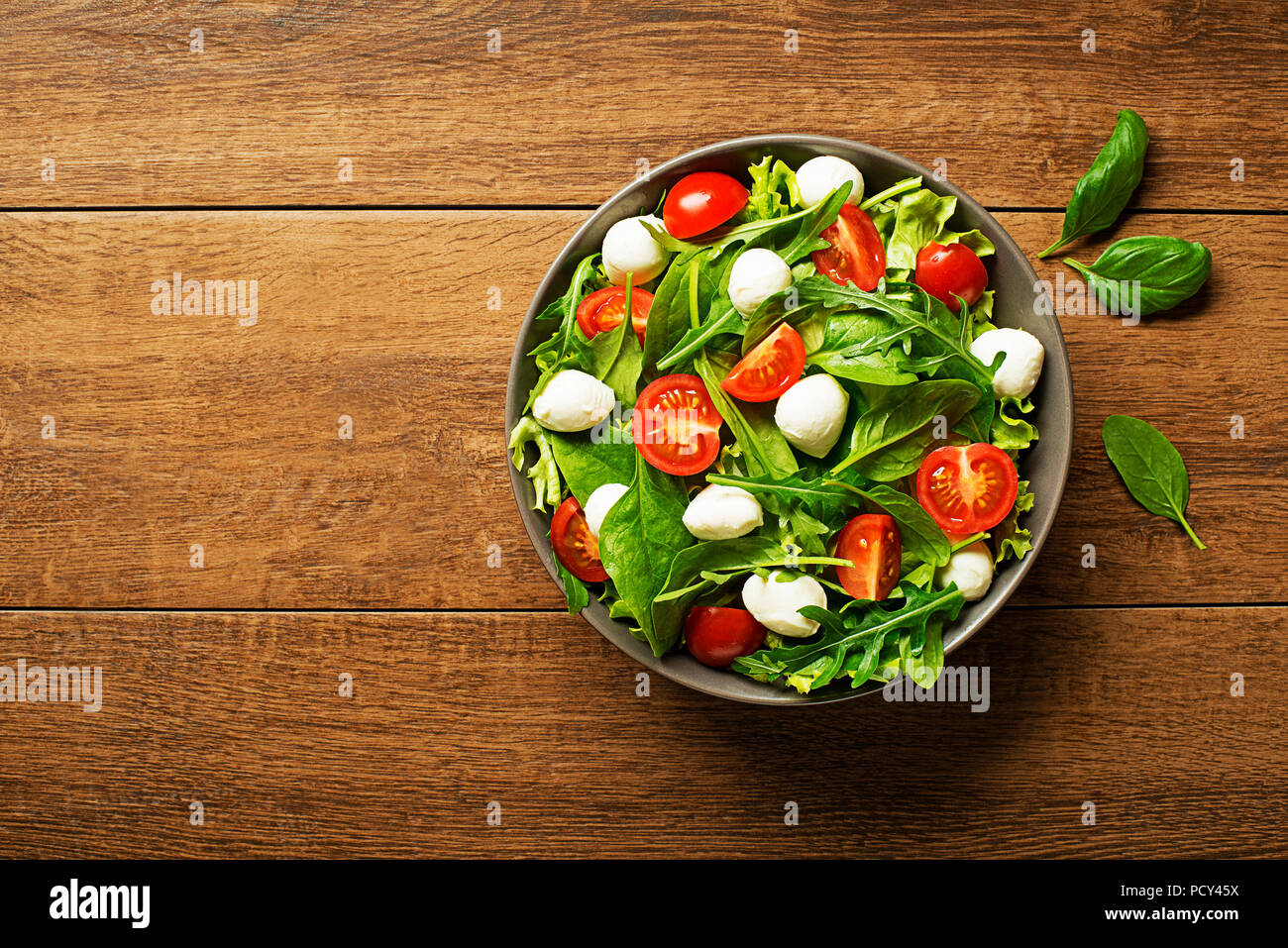 Green lettuce Salad with mozzarella cheese arugula and tomato on wooden background Stock Photo