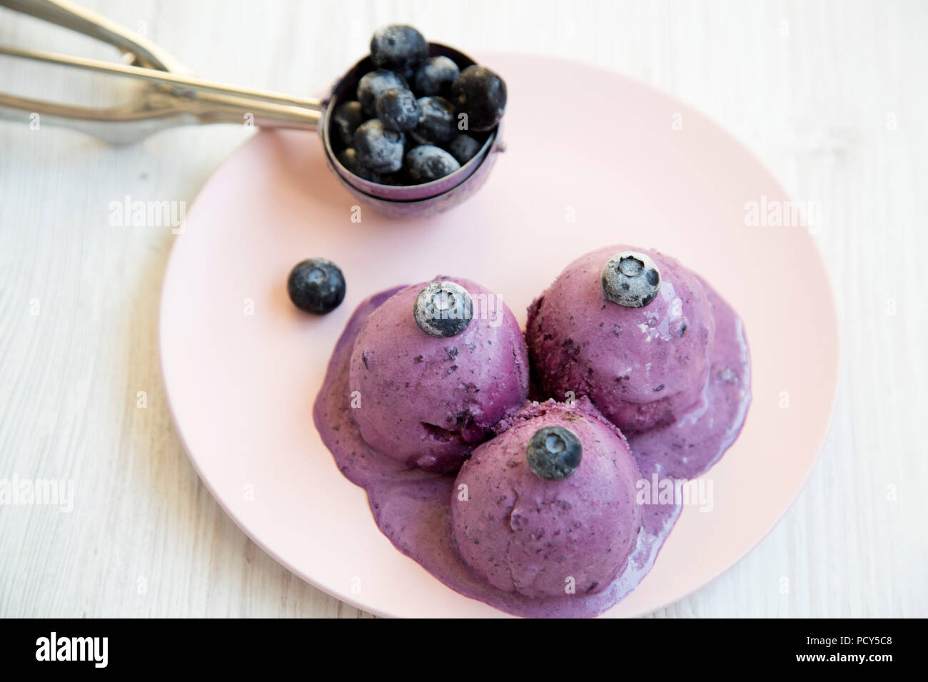 Blueberry ice cream balls with icecream scoop on a pink plate over white wooden suface, closeup. Stock Photo