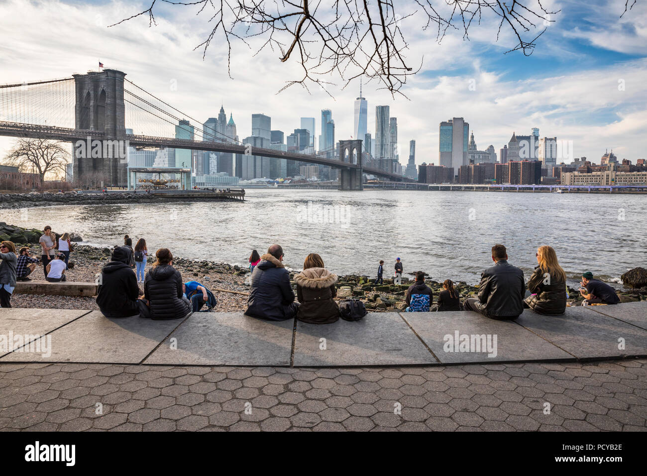 People sitting in DUMBO  and enjoying the view of Brooklyn Bridge and Downtown Manhattan in New York Stock Photo
