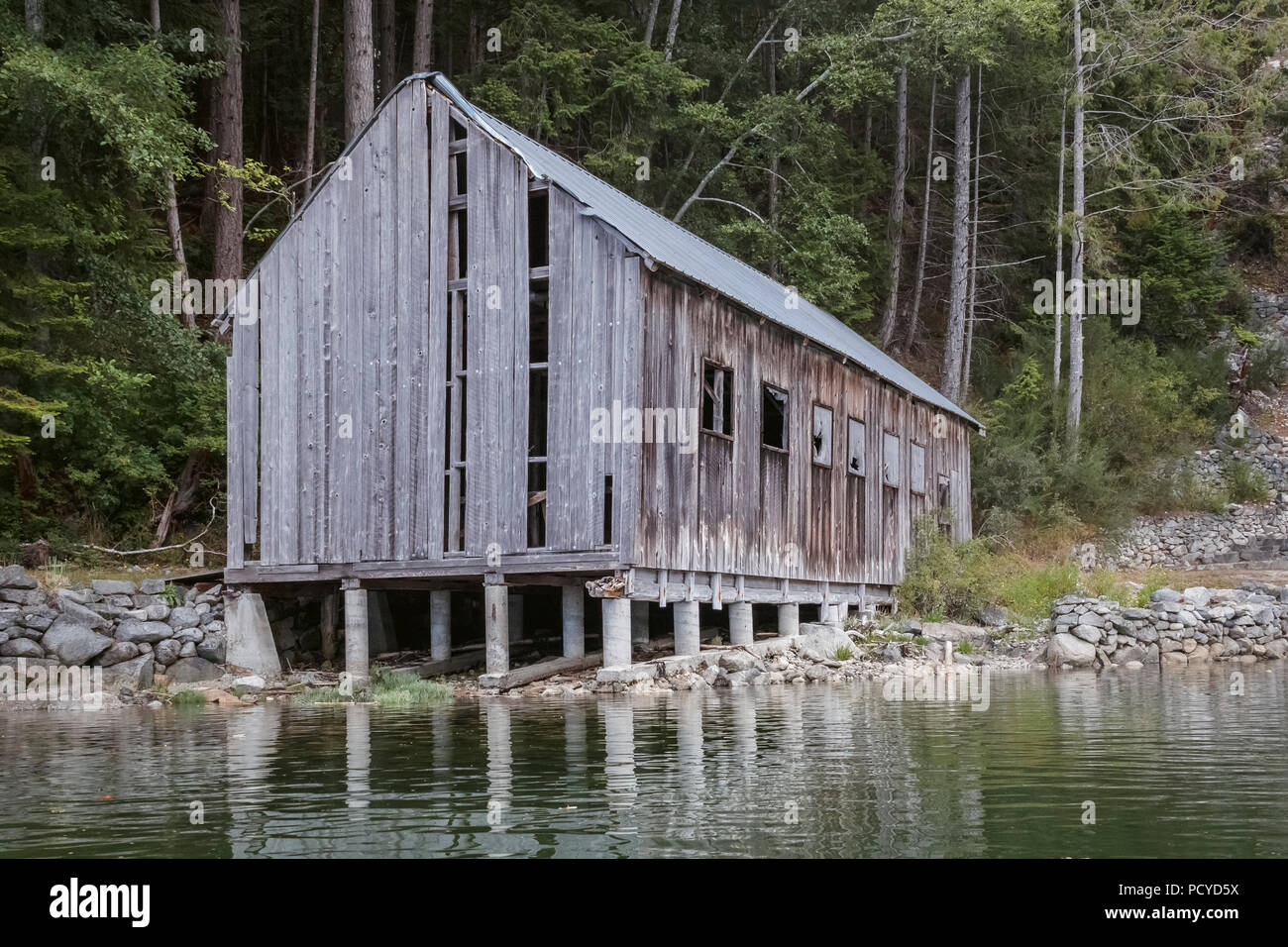 In need of repair, an old weathered wooden boat shed extends out from shore, standing on concrete supports that will be partly submerged at high tide. Stock Photo